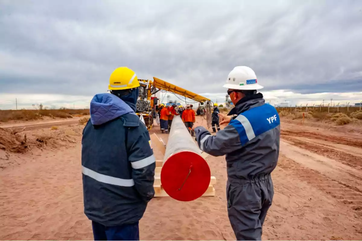 Trabajadores con cascos y equipo de seguridad supervisan la instalación de un gran tubo en un sitio de construcción al aire libre.