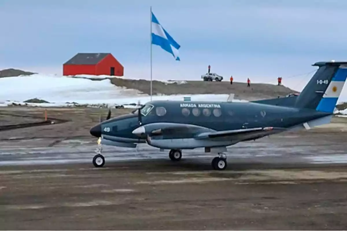 Un avión de la Armada Argentina en una pista con una bandera argentina ondeando y un edificio rojo en el fondo.