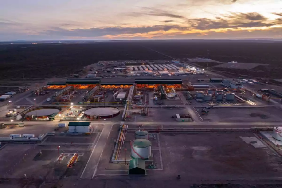 Vista aérea de una planta industrial al atardecer con estructuras iluminadas y tanques de almacenamiento.