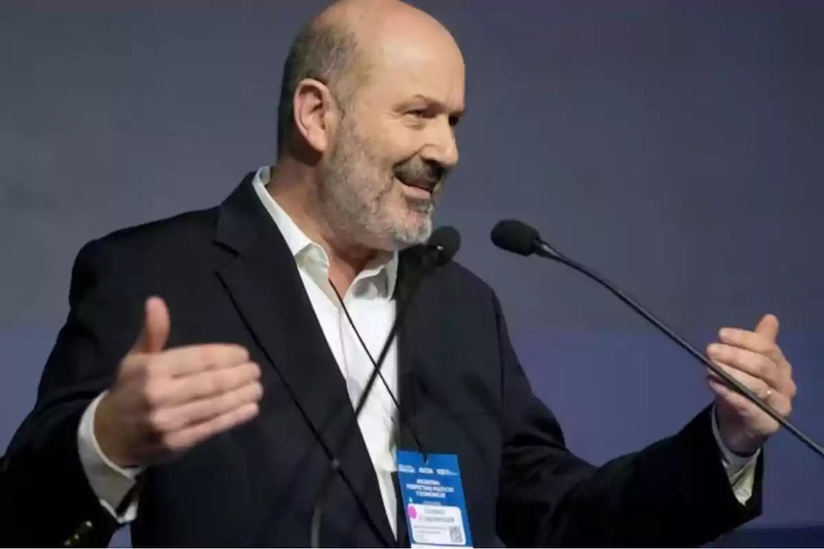 Hombre calvo con barba hablando en un micrófono durante una conferencia.