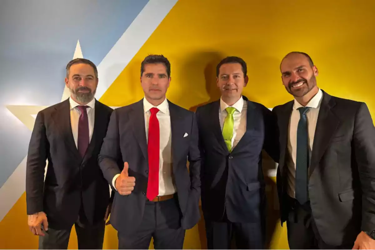 Cuatro hombres vestidos con trajes formales posan frente a una pared con un diseño de estrella.