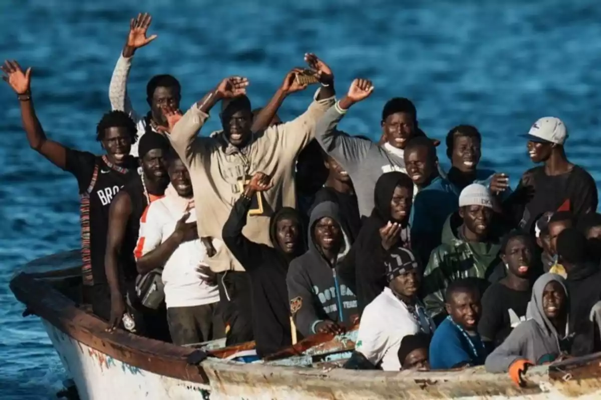 Un grupo de personas en un bote en el mar, algunas levantando los brazos y sonriendo.