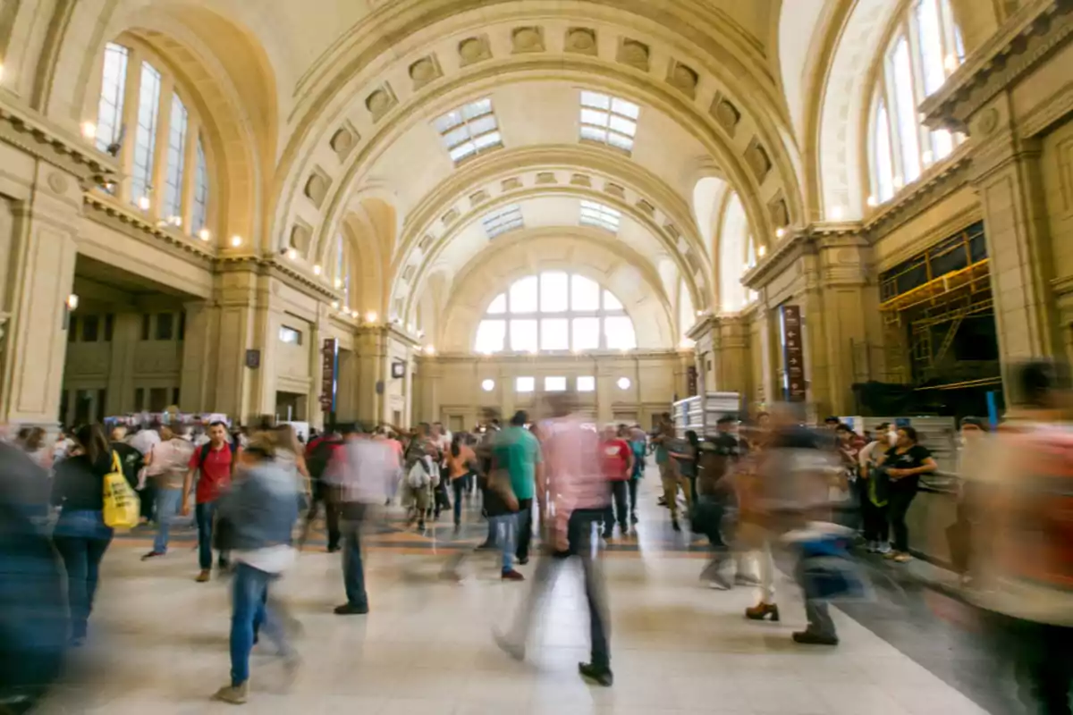 Personas caminando en el interior de una estación de tren con arquitectura clásica y techos altos.