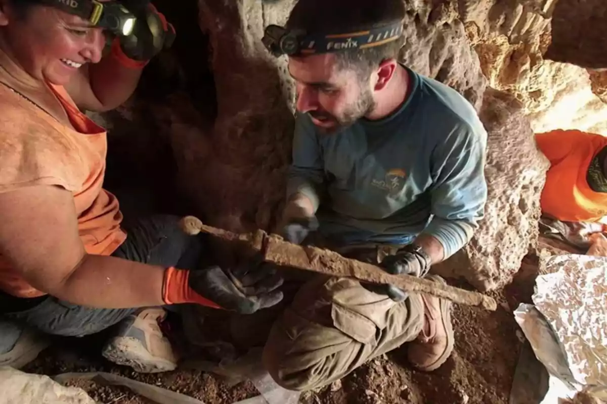 Dos personas en una cueva sostienen una espada antigua mientras usan linternas en la cabeza.