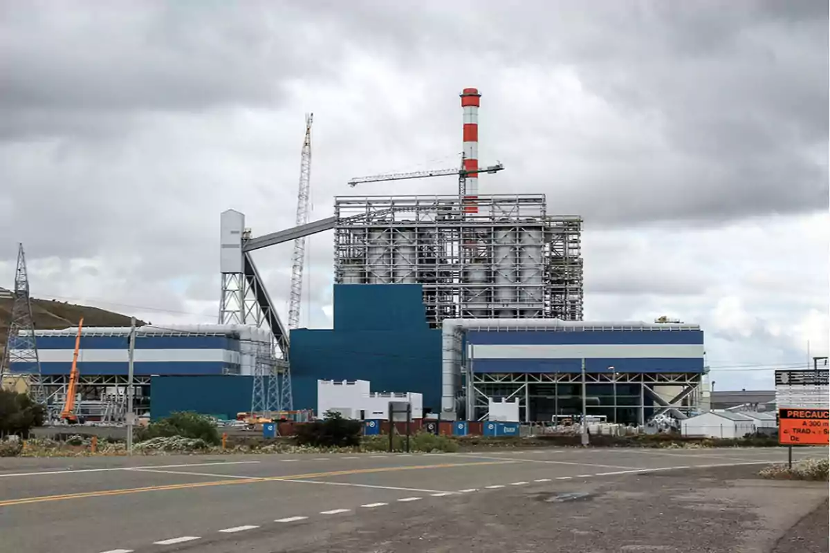 Una planta industrial con estructuras metálicas y una chimenea alta en un día nublado.