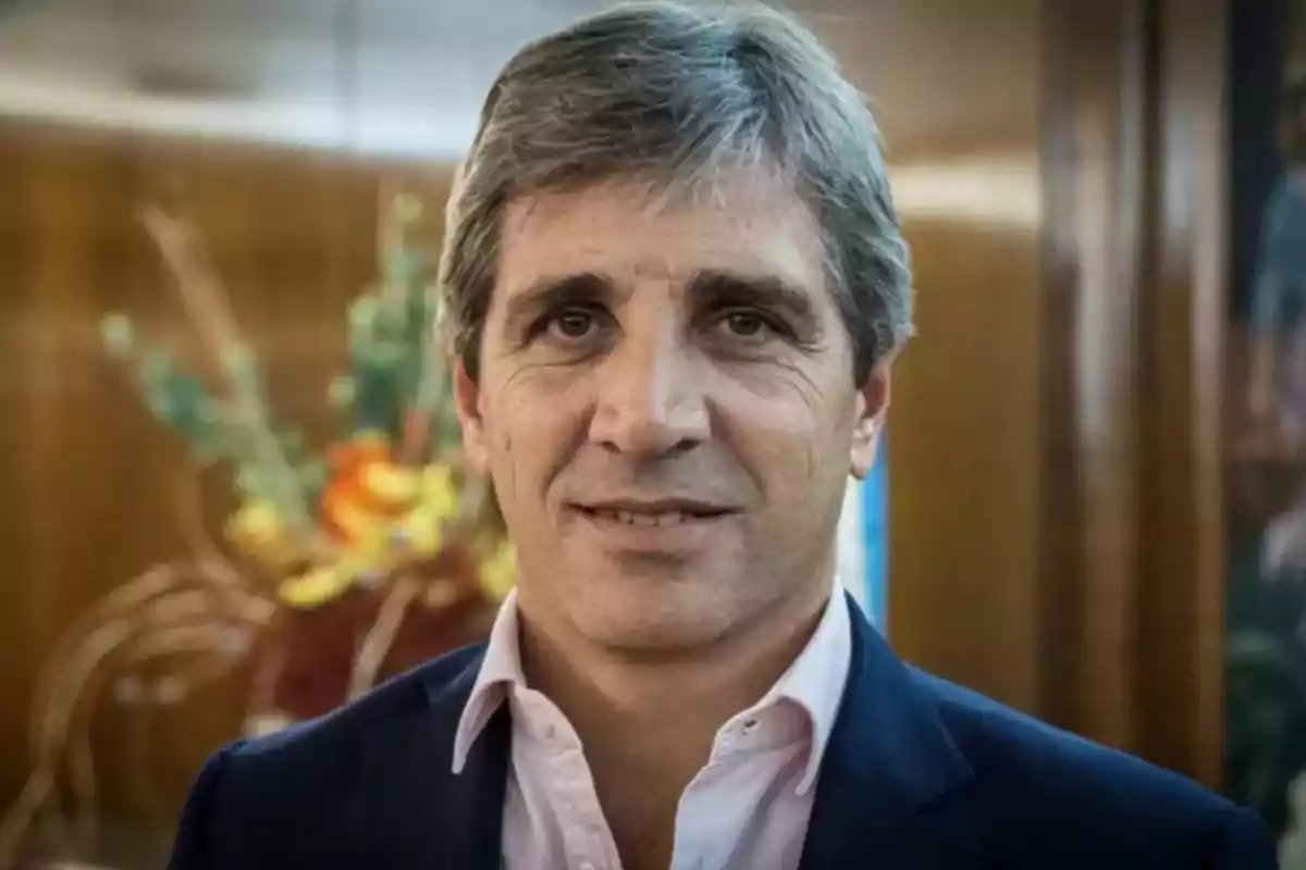 Un hombre de cabello canoso y traje oscuro sonríe frente a una decoración floral en un entorno interior.