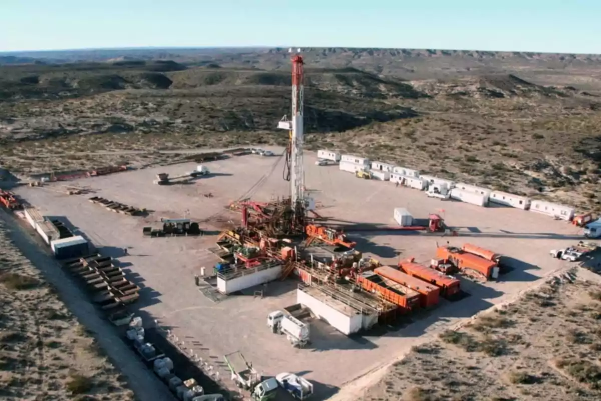 Plataforma de perforación en un campo petrolero rodeado de equipos y vehículos en un paisaje árido.