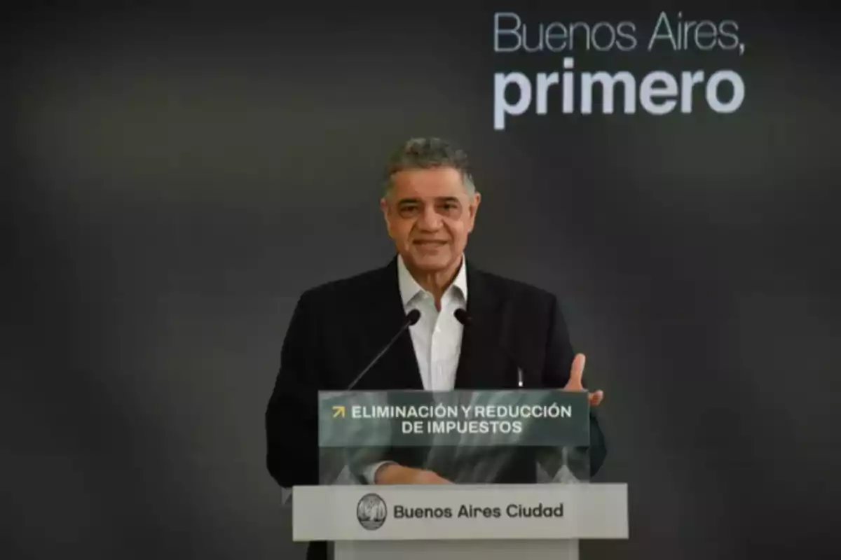 Un hombre hablando en un podio con el texto "Buenos Aires primero" y "Eliminación y reducción de impuestos" en el fondo.