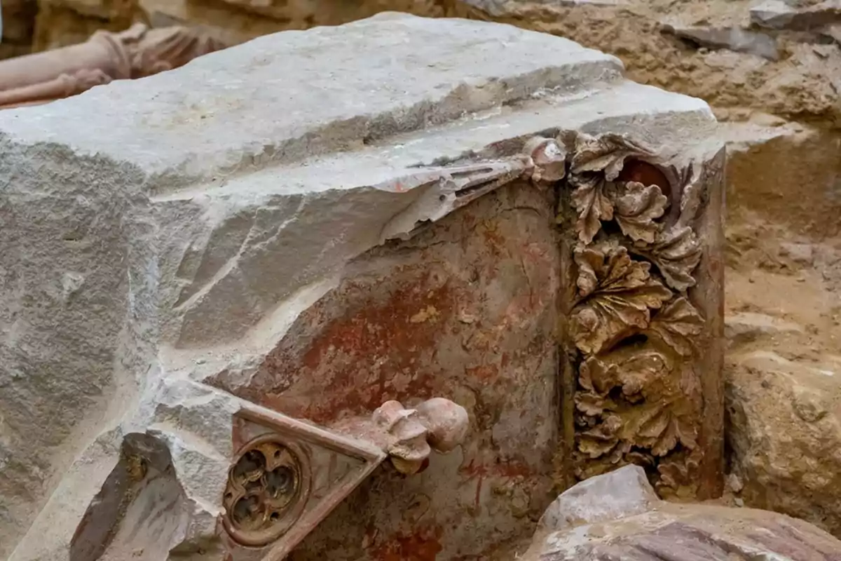 Detalle de un relieve en piedra con motivos florales y decorativos en un entorno de excavación arqueológica.