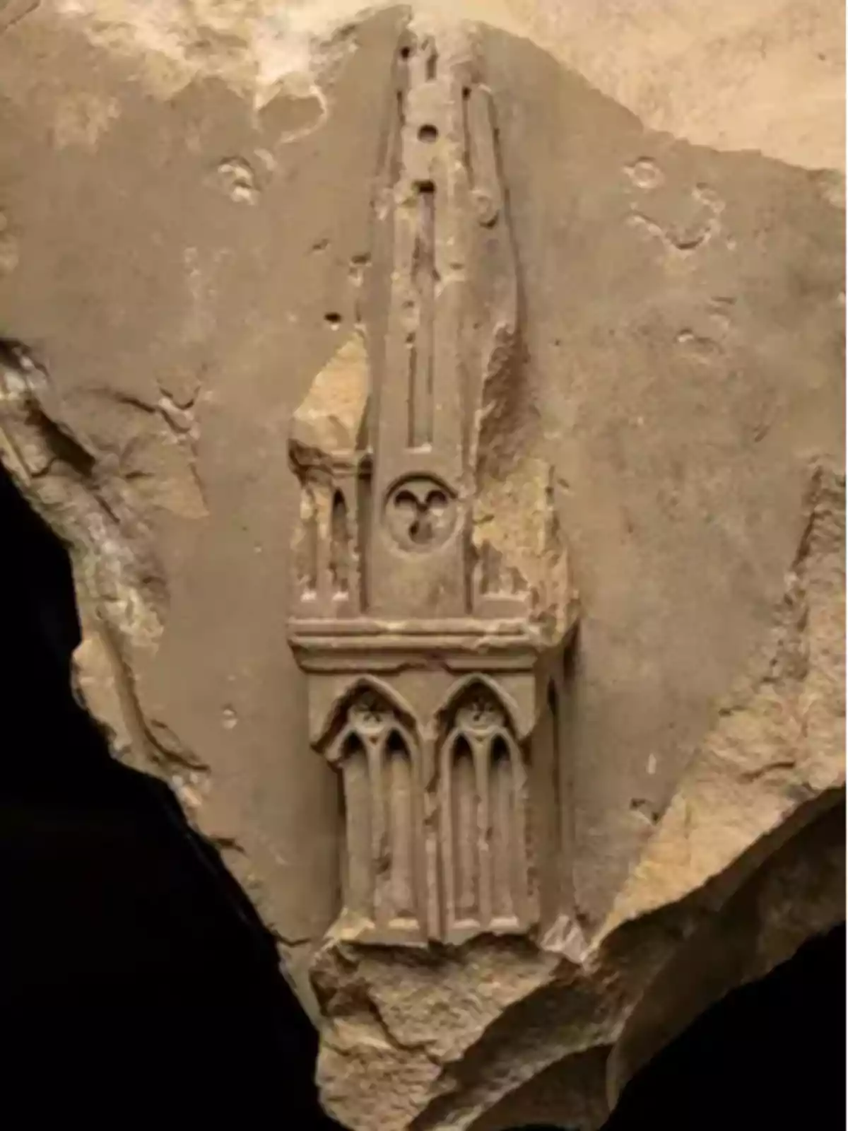 Fragmento de piedra con un relieve que muestra una estructura arquitectónica gótica con arcos y detalles ornamentales.