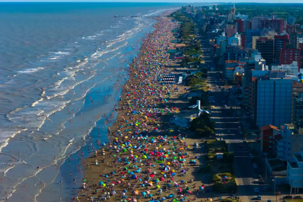 Vista aérea de una playa concurrida con muchas sombrillas coloridas y edificios a lo largo de la costa.