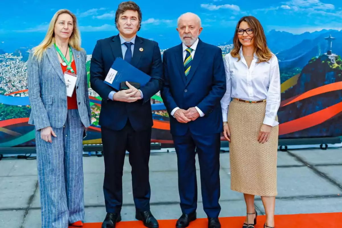 Cuatro personas posan juntas en un evento formal con un fondo que muestra un paisaje urbano y montañoso.