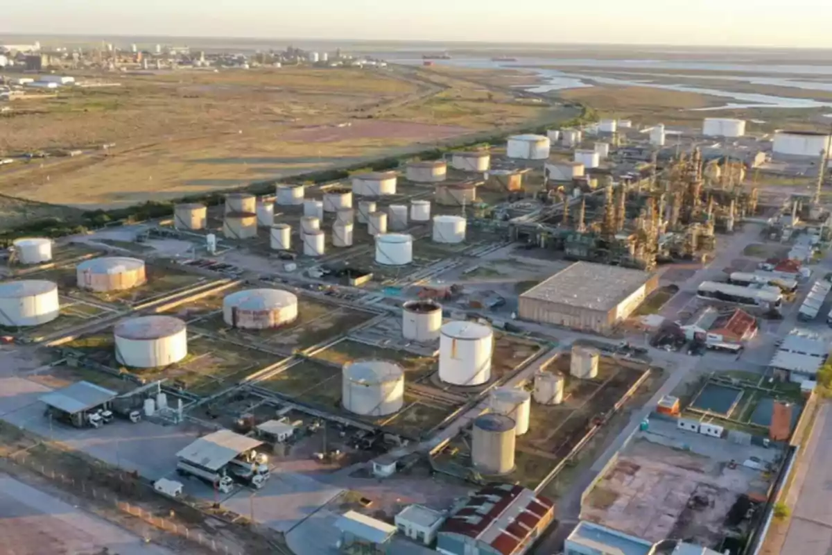 Vista aérea de una refinería de petróleo con múltiples tanques de almacenamiento y estructuras industriales en un paisaje amplio y despejado.