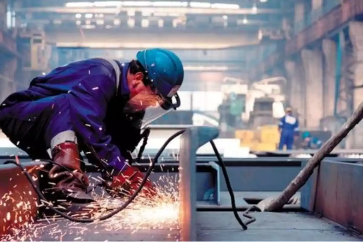 Trabajador con casco y equipo de protección realizando tareas de soldadura en una fábrica.