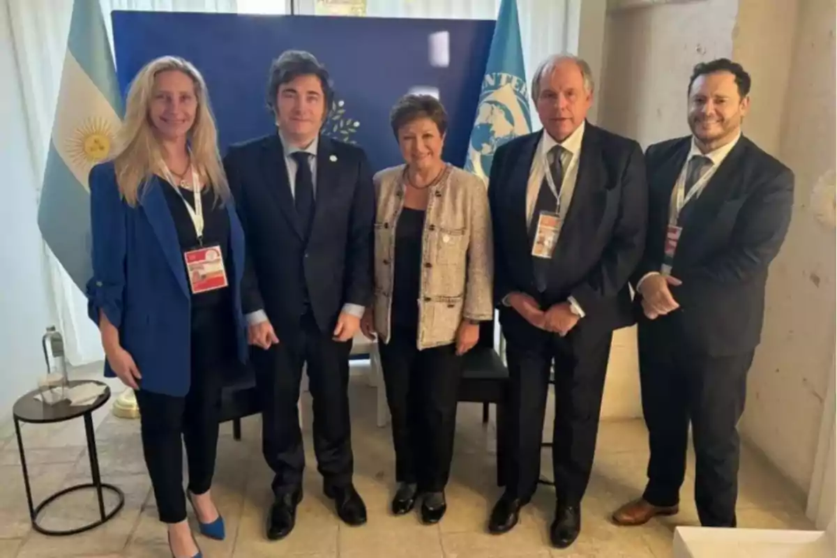 Cinco personas posan juntas en un evento formal con banderas de Argentina y otra organización de fondo.