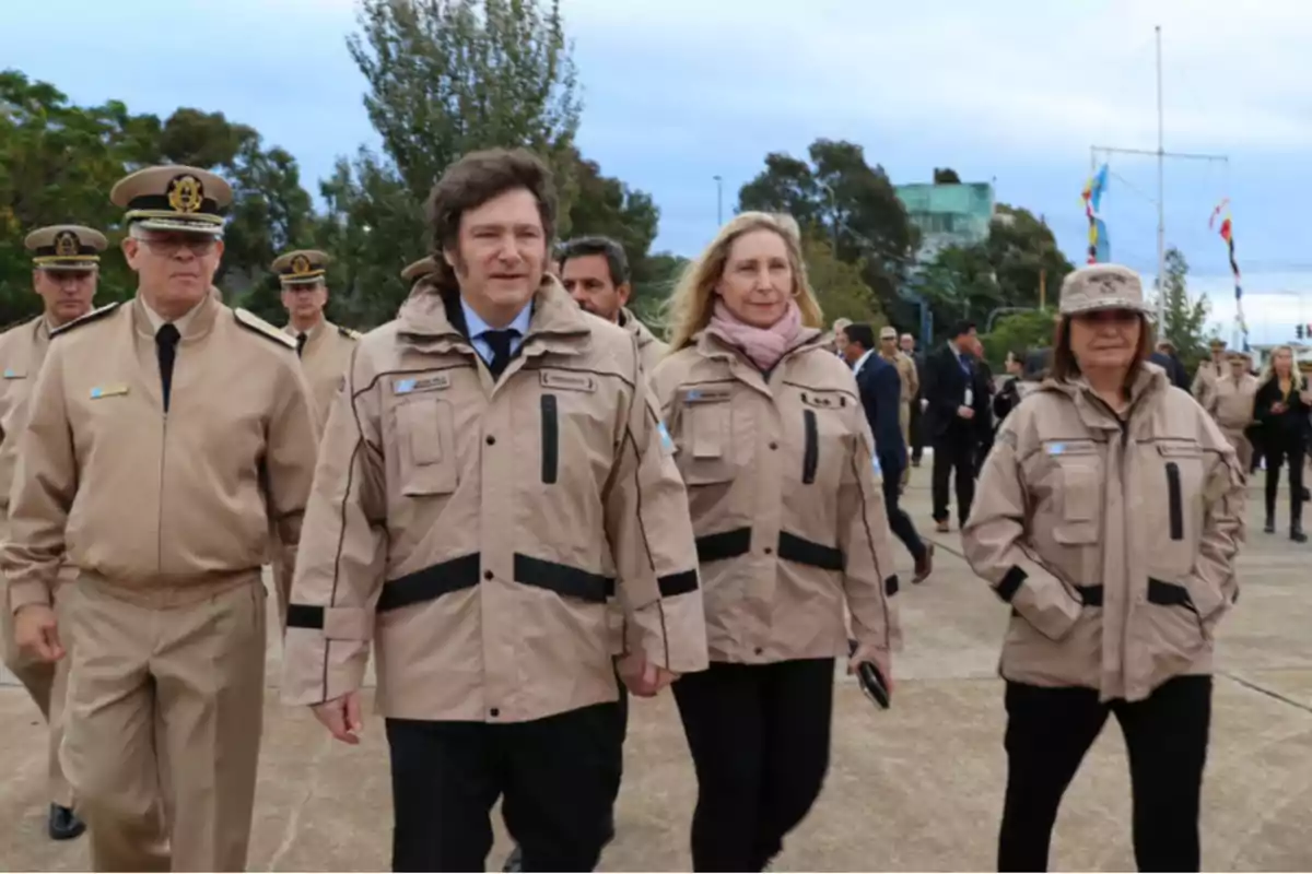 Un grupo de personas vestidas con uniformes beige caminan al aire libre en un evento formal.