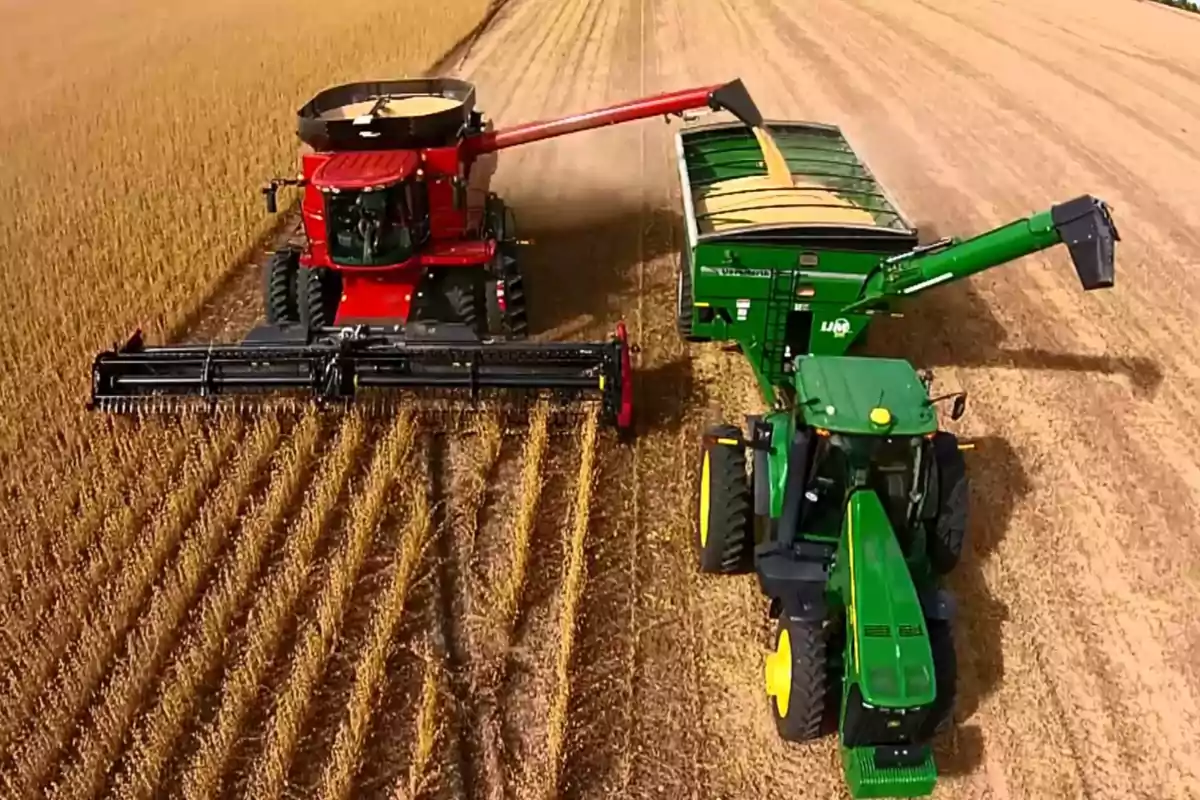 Una cosechadora roja y un tractor verde trabajando juntos en un campo de cultivo.