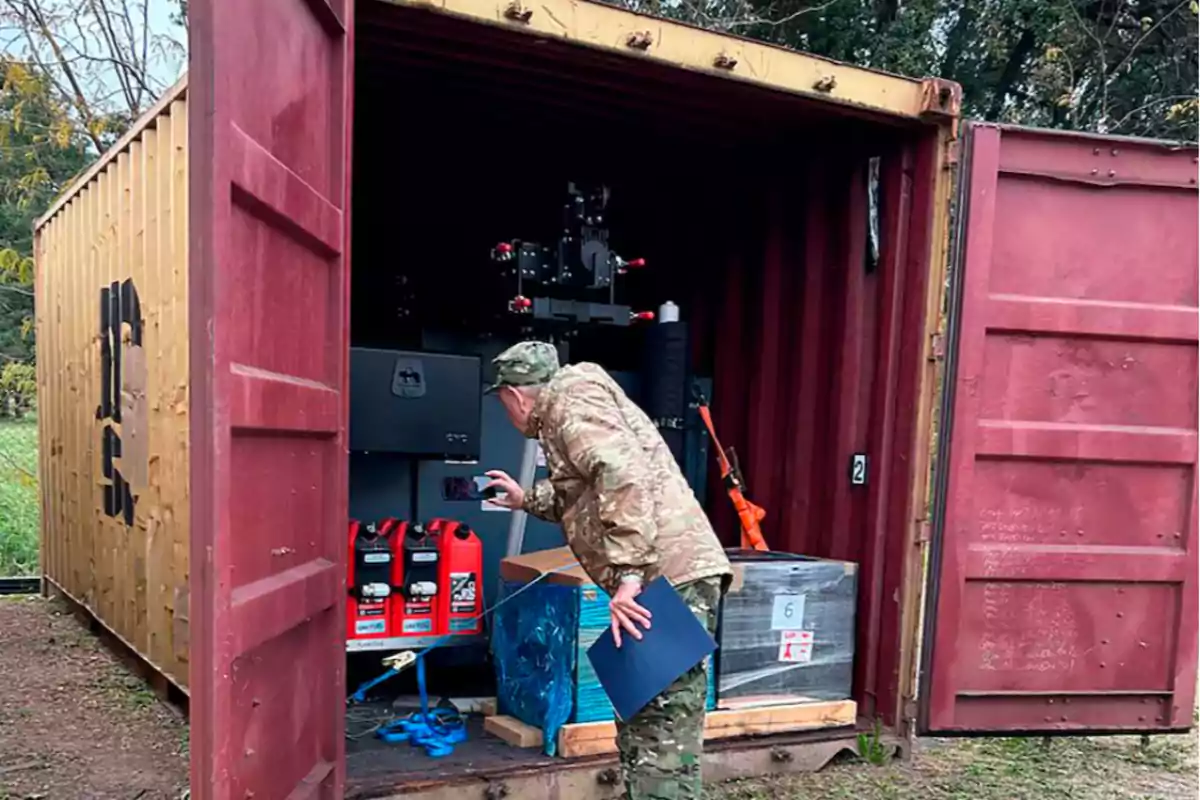 Un hombre con uniforme militar inspecciona el interior de un contenedor abierto que contiene varios equipos y materiales.