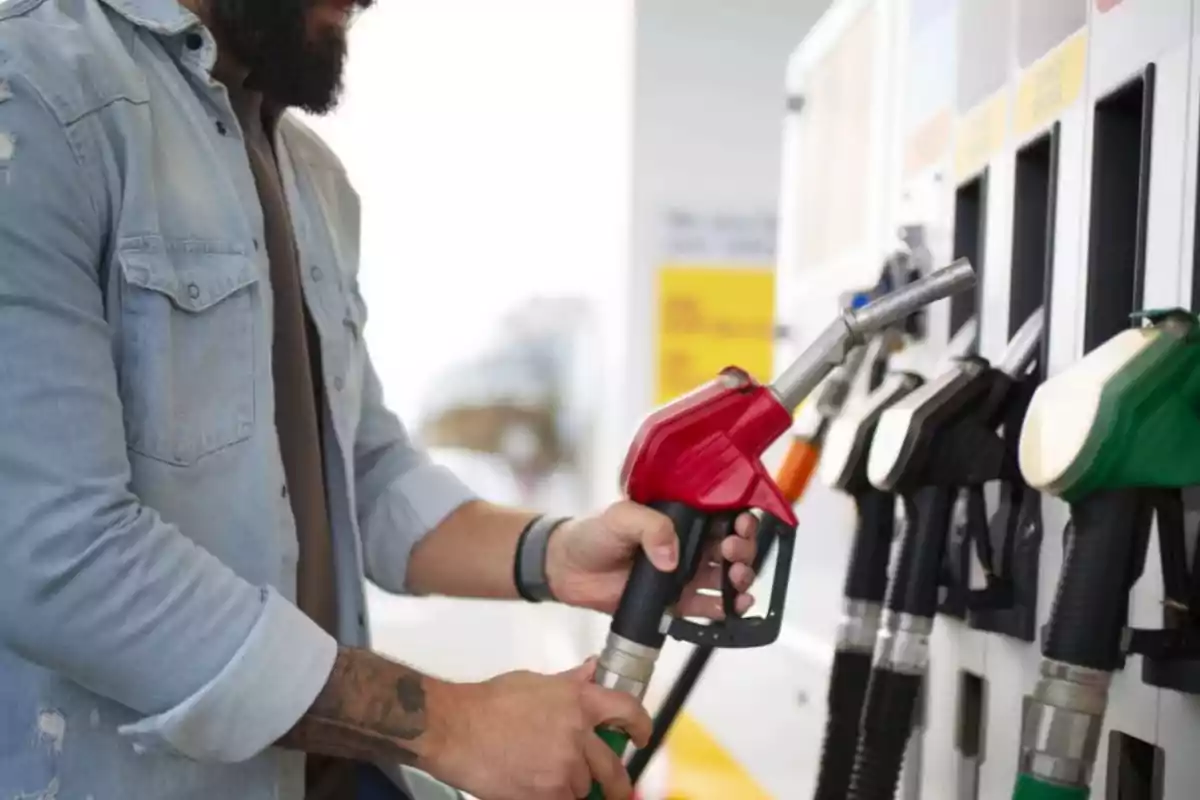 Persona llenando el tanque de un vehículo en una estación de servicio con una manguera de combustible roja.