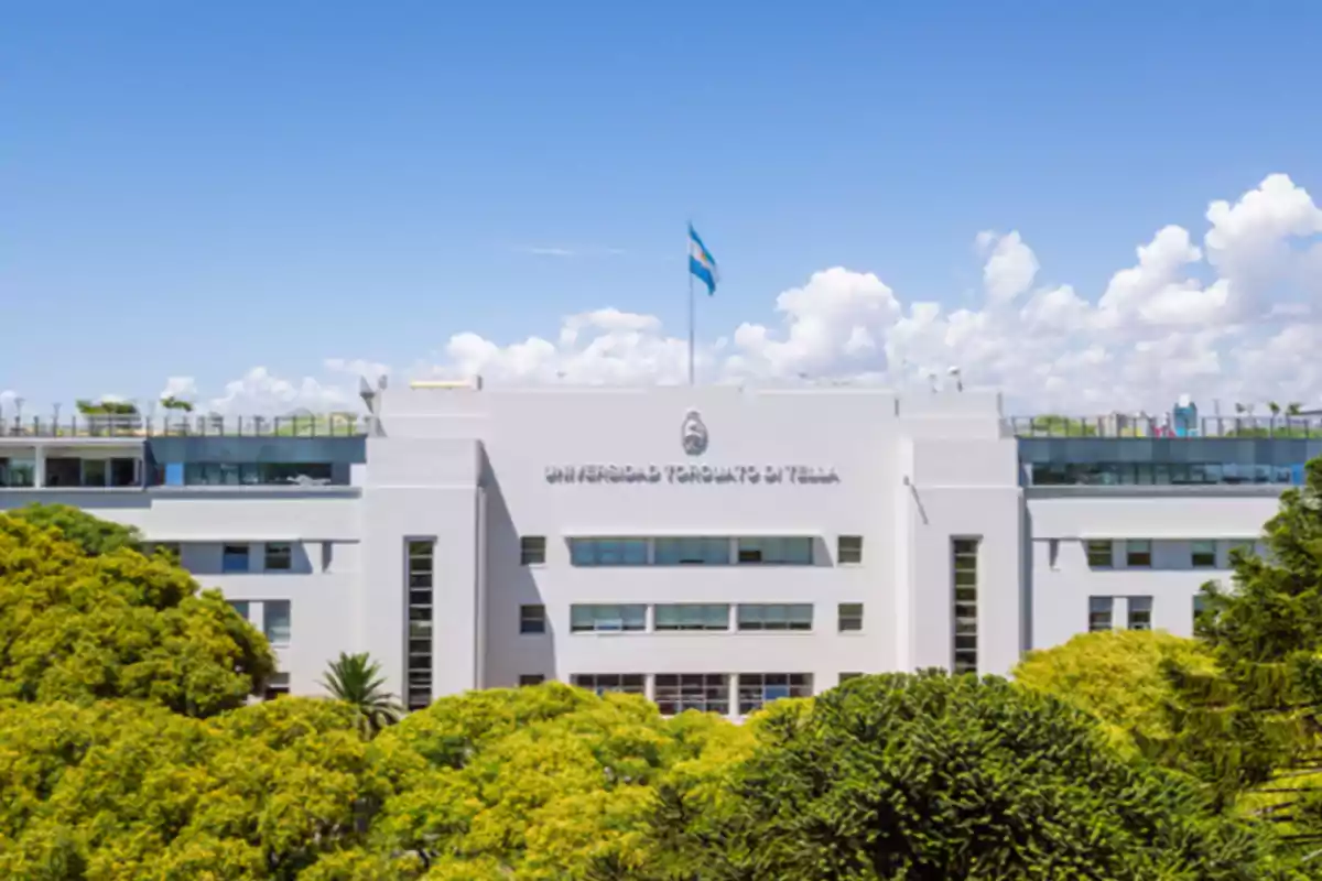 Edificio blanco de la Universidad Torcuato Di Tella con árboles en primer plano y cielo azul de fondo.