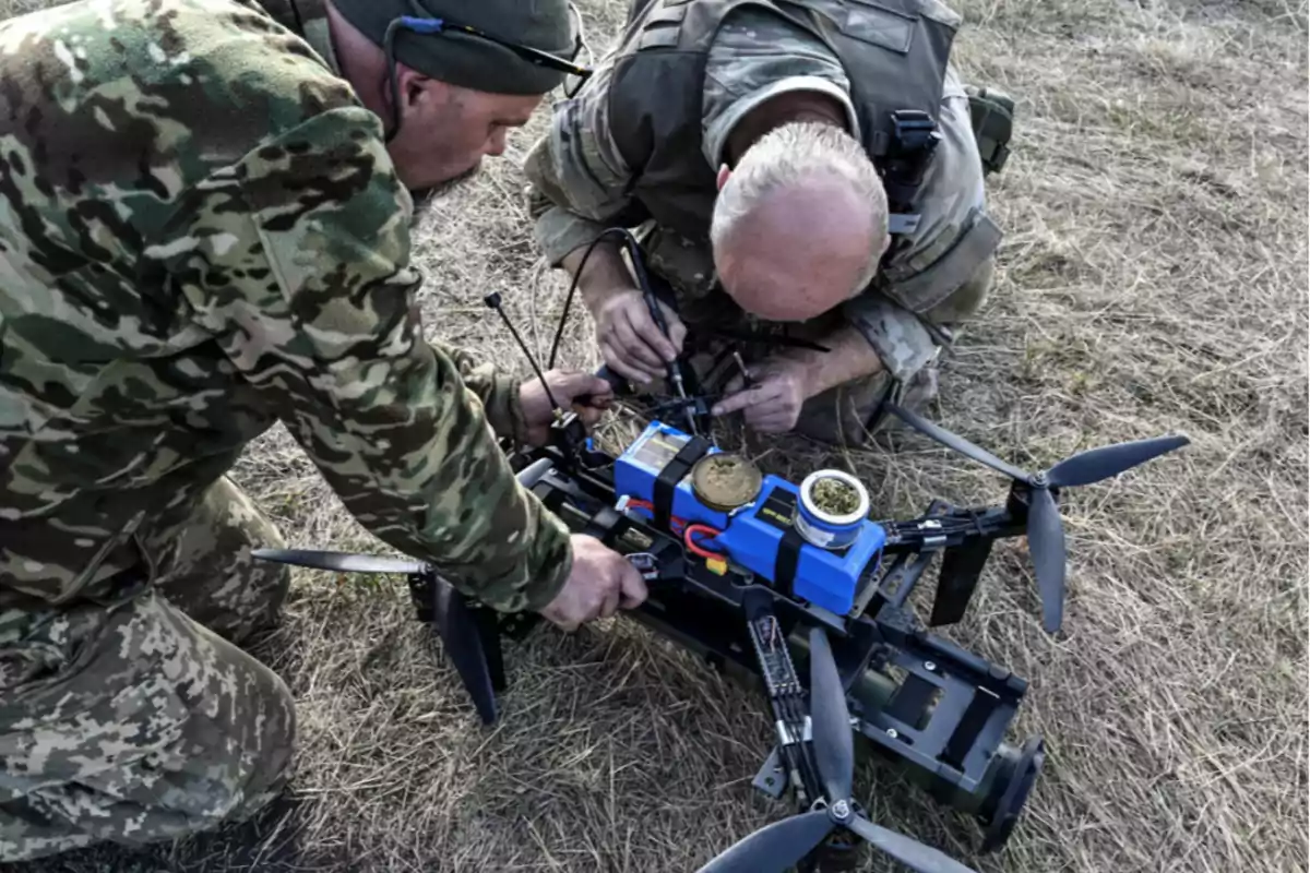 Dos personas en uniforme militar trabajan en un dron en un campo.