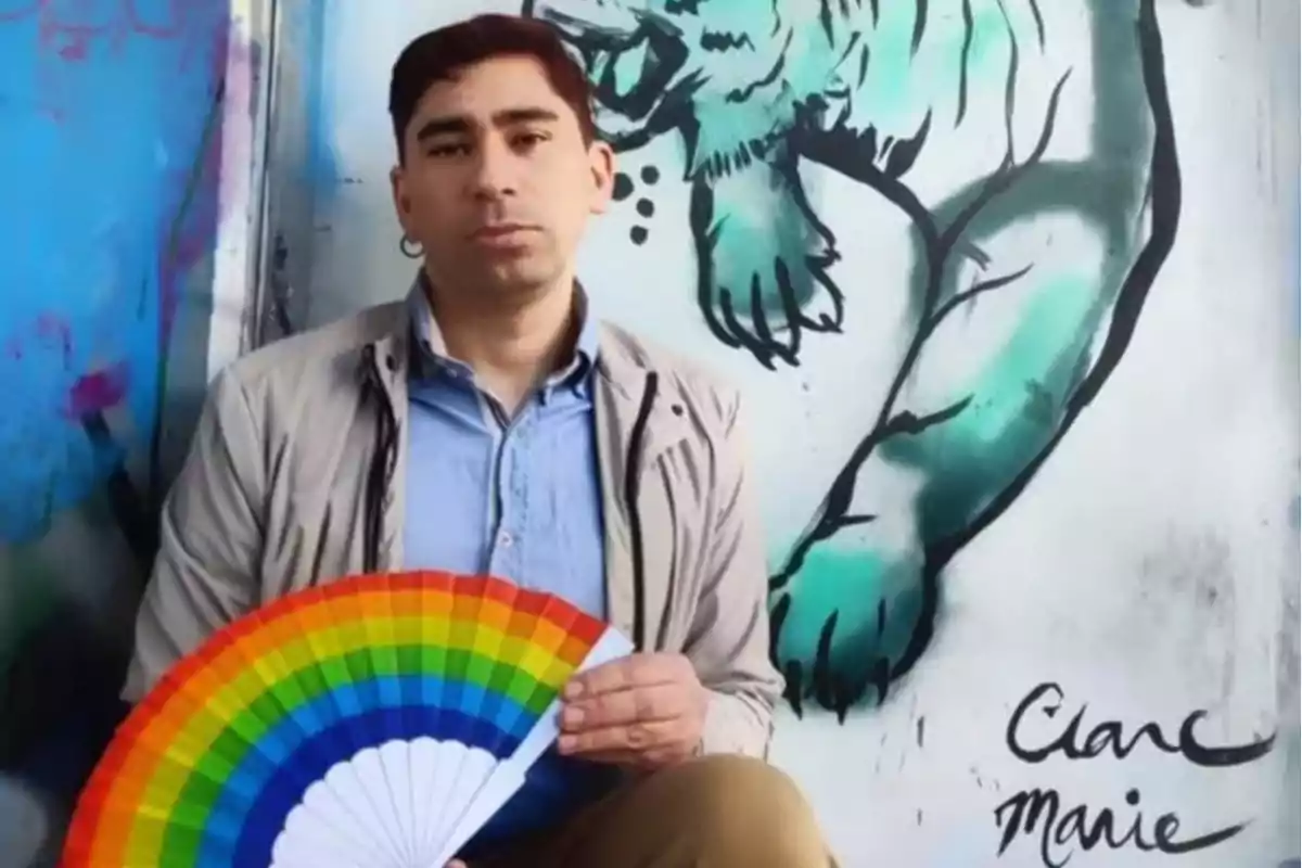 Un hombre sostiene un abanico con los colores del arcoíris frente a un mural de un oso polar.