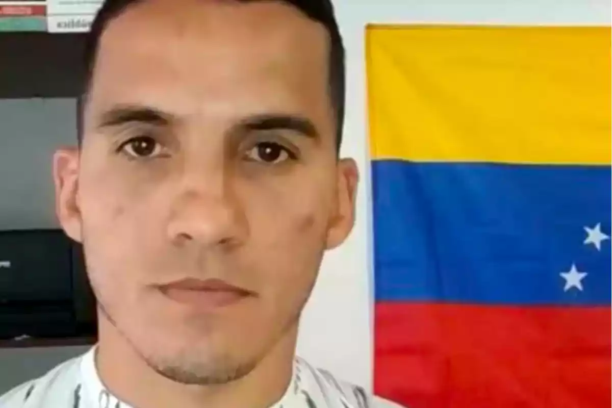 Un hombre de pie frente a una bandera de Venezuela.