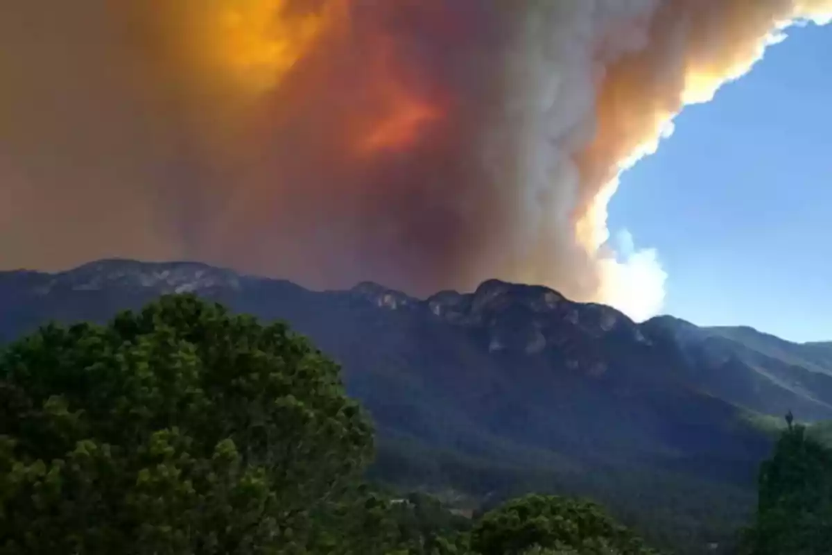 Mountains with a large wildfire in the background and thick smoke rising into the sky.