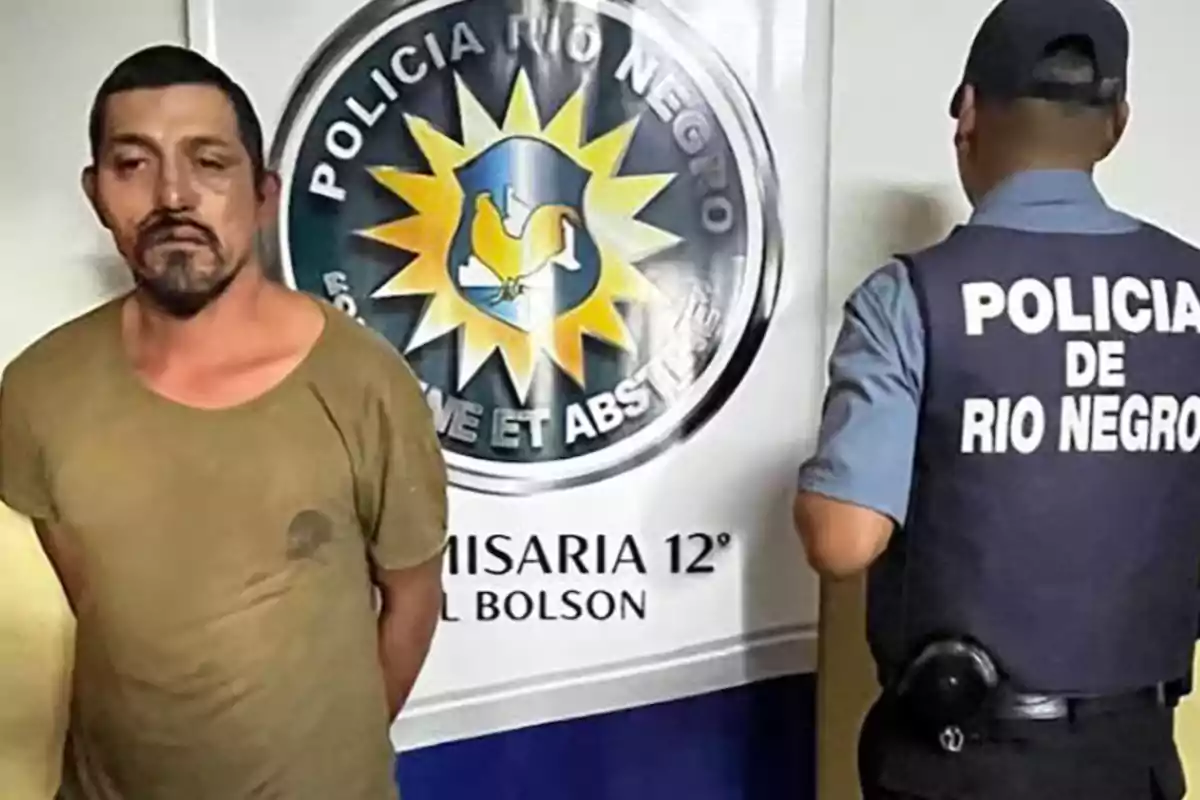 Un hombre de pie junto a un oficial de policía frente a un cartel de la Policía de Río Negro.