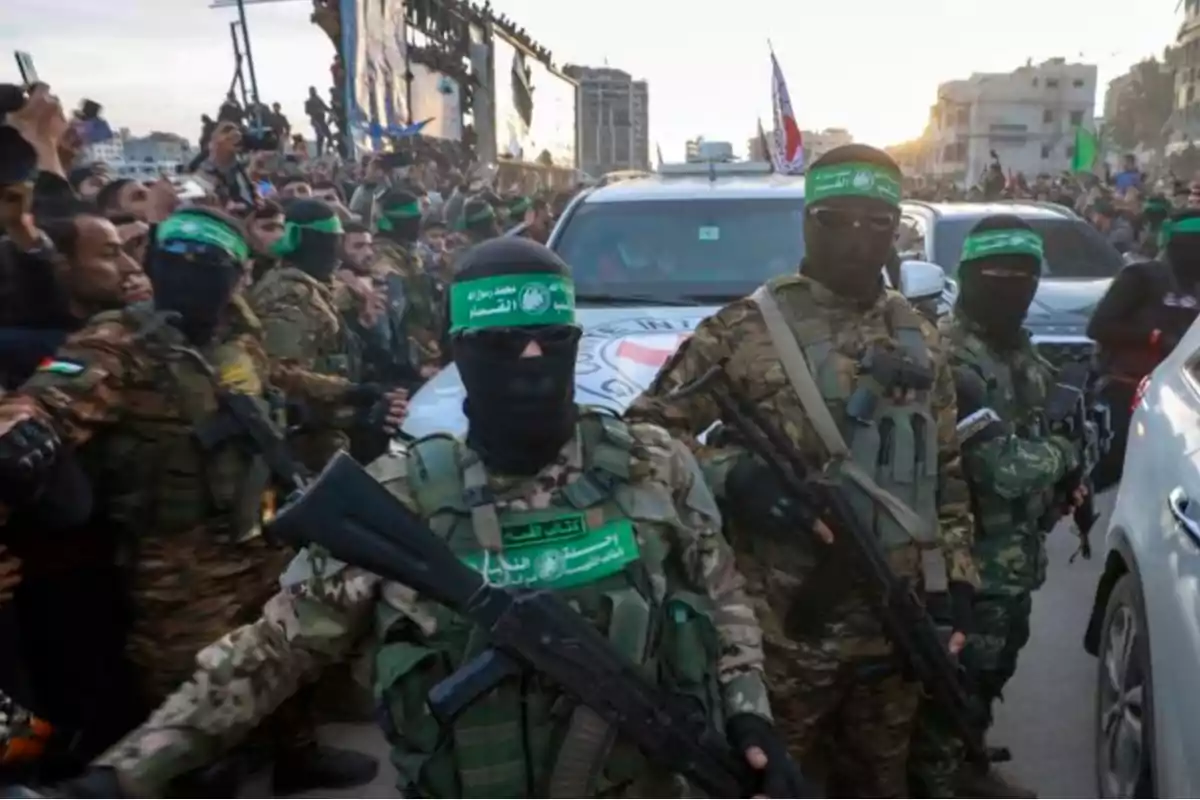 Un grupo de personas armadas con uniformes militares y pasamontañas verdes rodea un vehículo en una calle llena de gente.