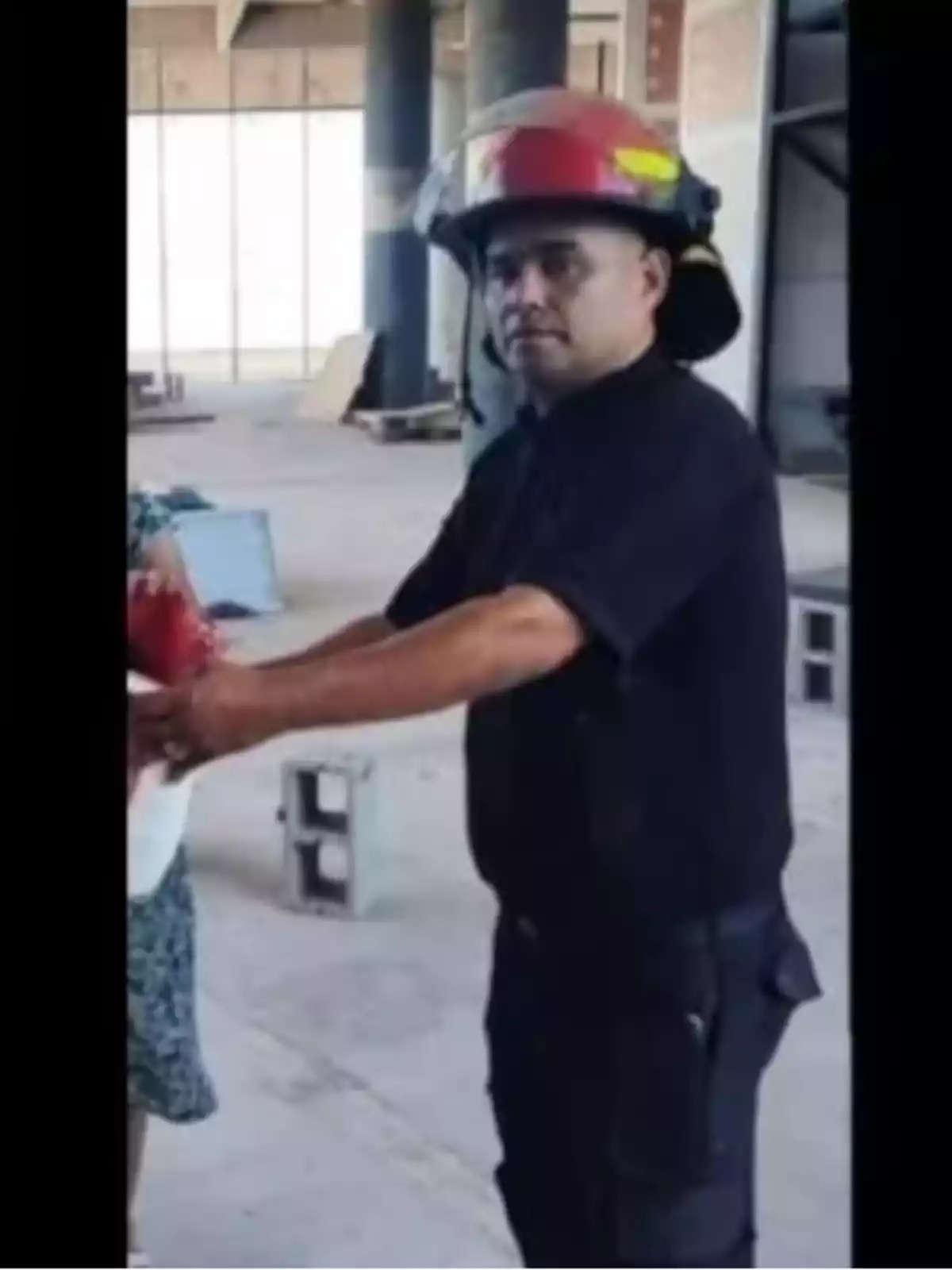 Un bombero con casco rojo sostiene un objeto en un edificio en construcción.