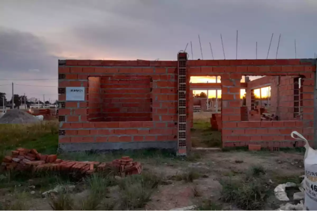 Construcción de una casa en proceso con paredes de ladrillo y un atardecer al fondo.