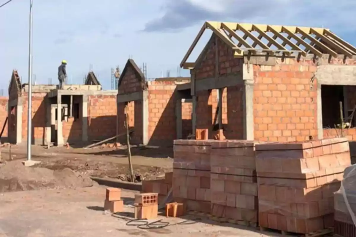 Construcción de casas de ladrillo con un trabajador en el techo y materiales apilados en el suelo.