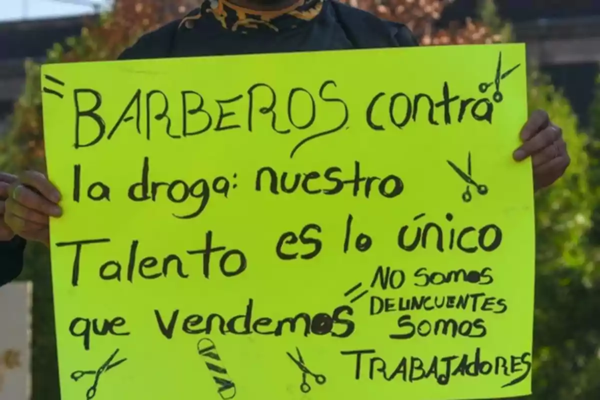 Person holding a yellow sign that says "Barbers Against Drugs: Our Talent Is the Only Thing We Sell. We Are Not Criminals, We Are Workers," decorated with drawings of scissors and a barber's razor.