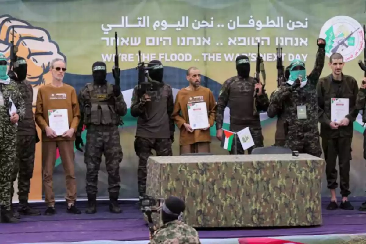 Un grupo de personas en uniforme militar y con armas posan junto a otros individuos que sostienen documentos, frente a un fondo con texto en varios idiomas.