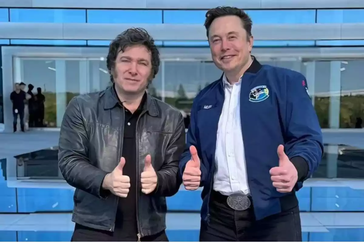 Two people pose in front of a modern building with glass windows, both wearing jackets and giving thumbs-up gestures.