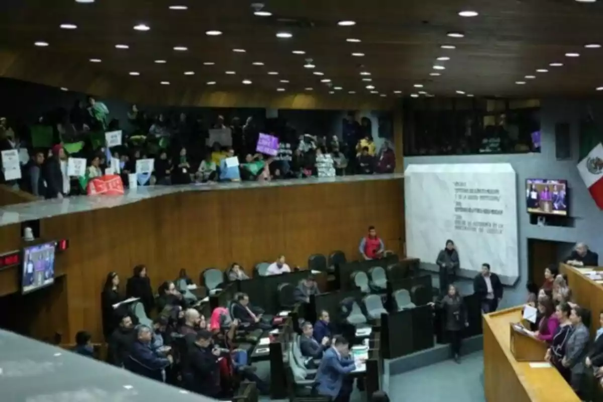 An assembly hall with people sitting and standing, some holding signs, while a formal session or meeting is taking place.