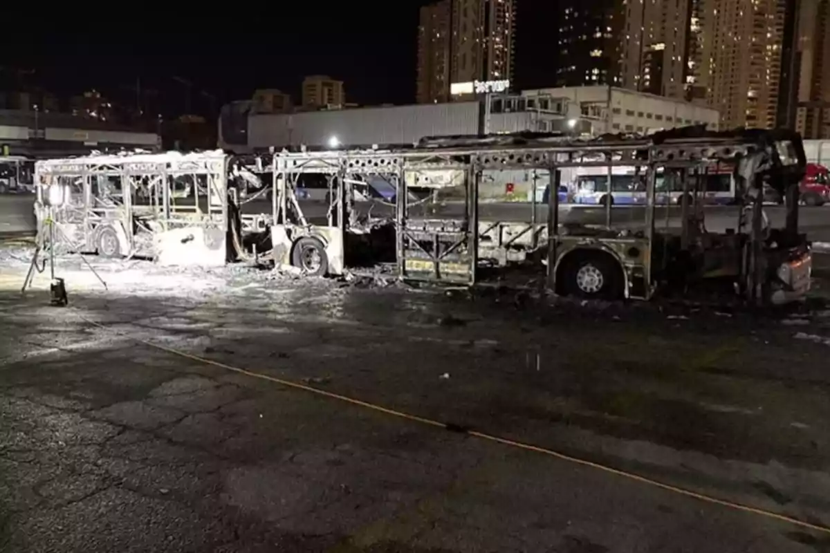 A completely burned bus in an urban parking lot overnight.