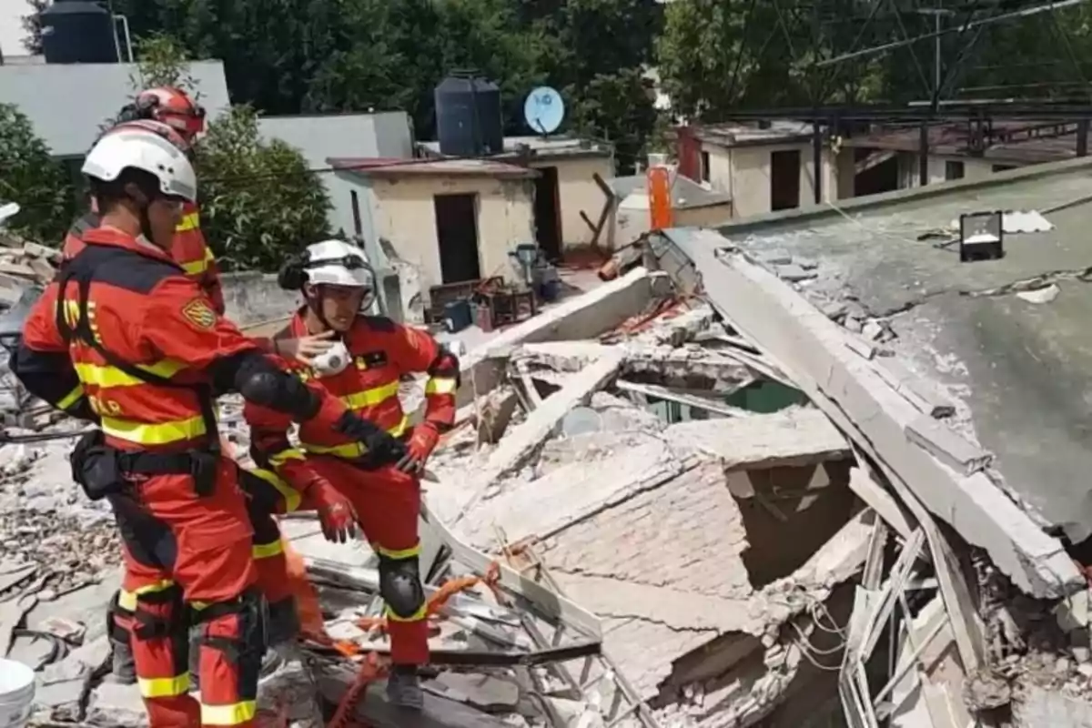 Rescatistas con uniformes rojos y cascos blancos inspeccionan los escombros de un edificio colapsado.