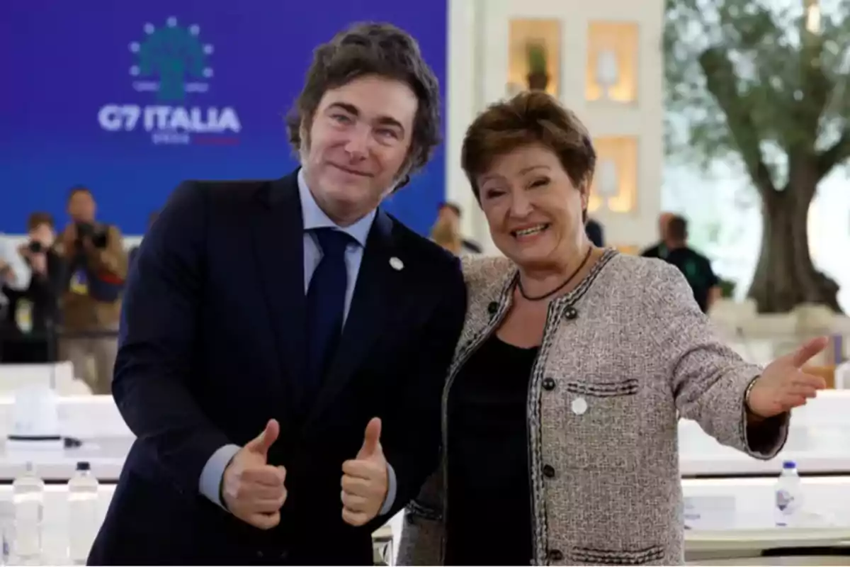 Two people pose smiling at a G7 event in Italy, one of them giving a thumbs-up gesture.