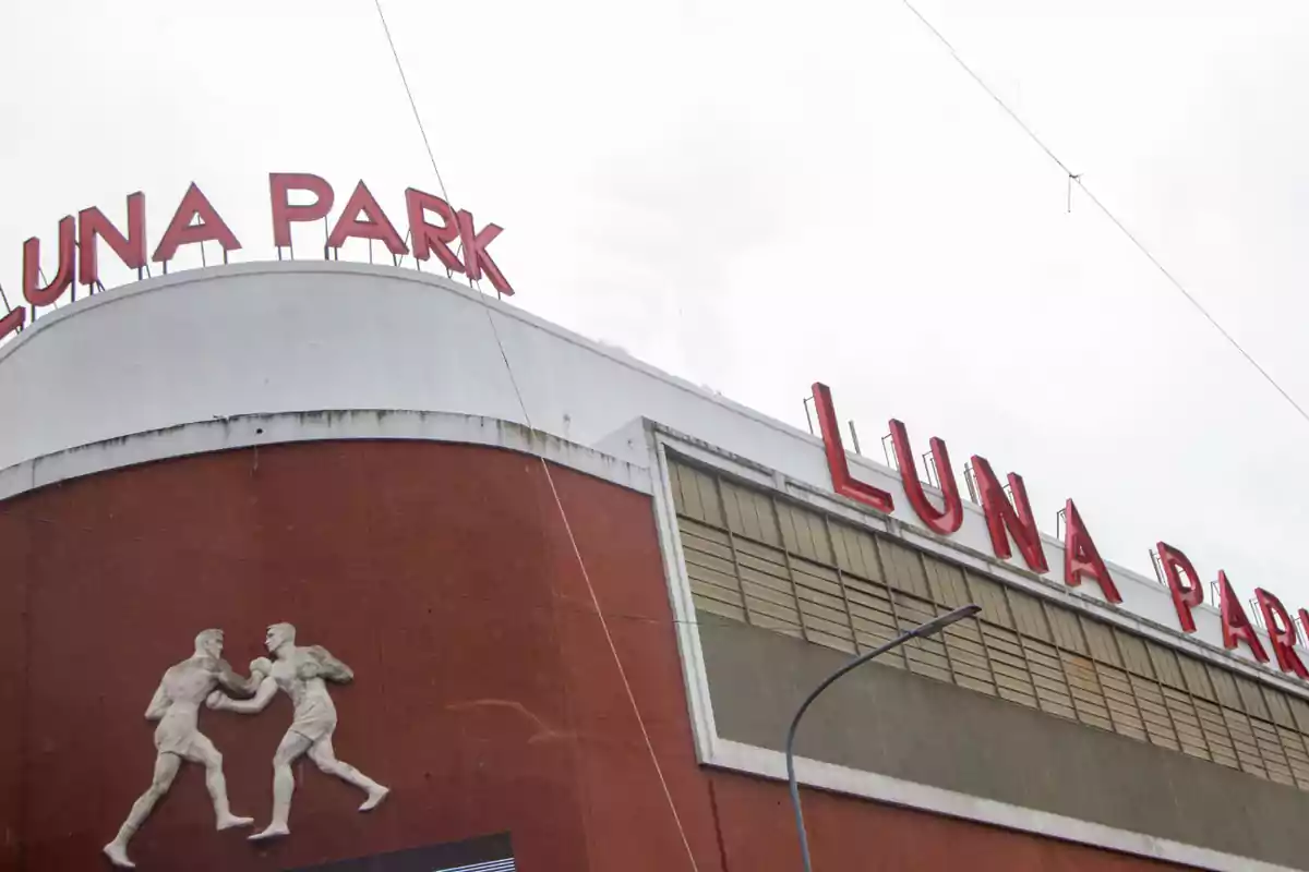 The image shows the facade of a building with the sign "Luna Park" in red letters and a sculpture of two boxers in relief on a brown wall.