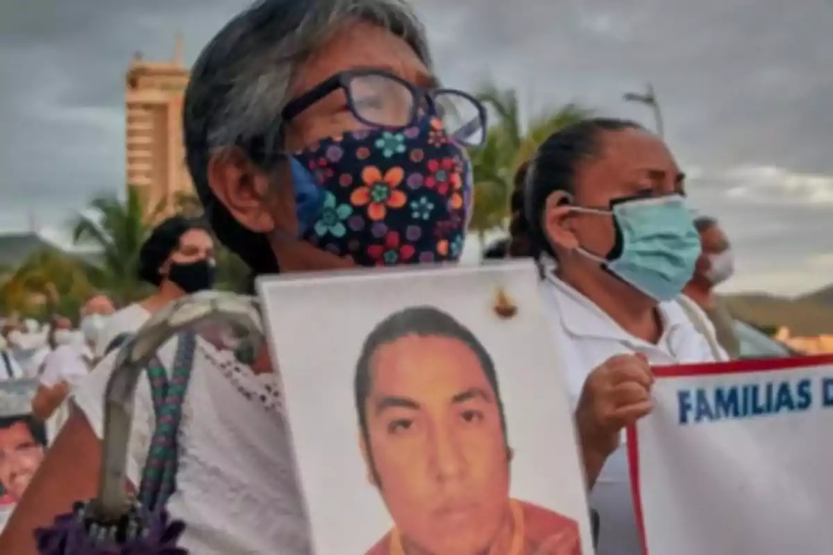 Una mujer con mascarilla sostiene una fotografía durante una manifestación.