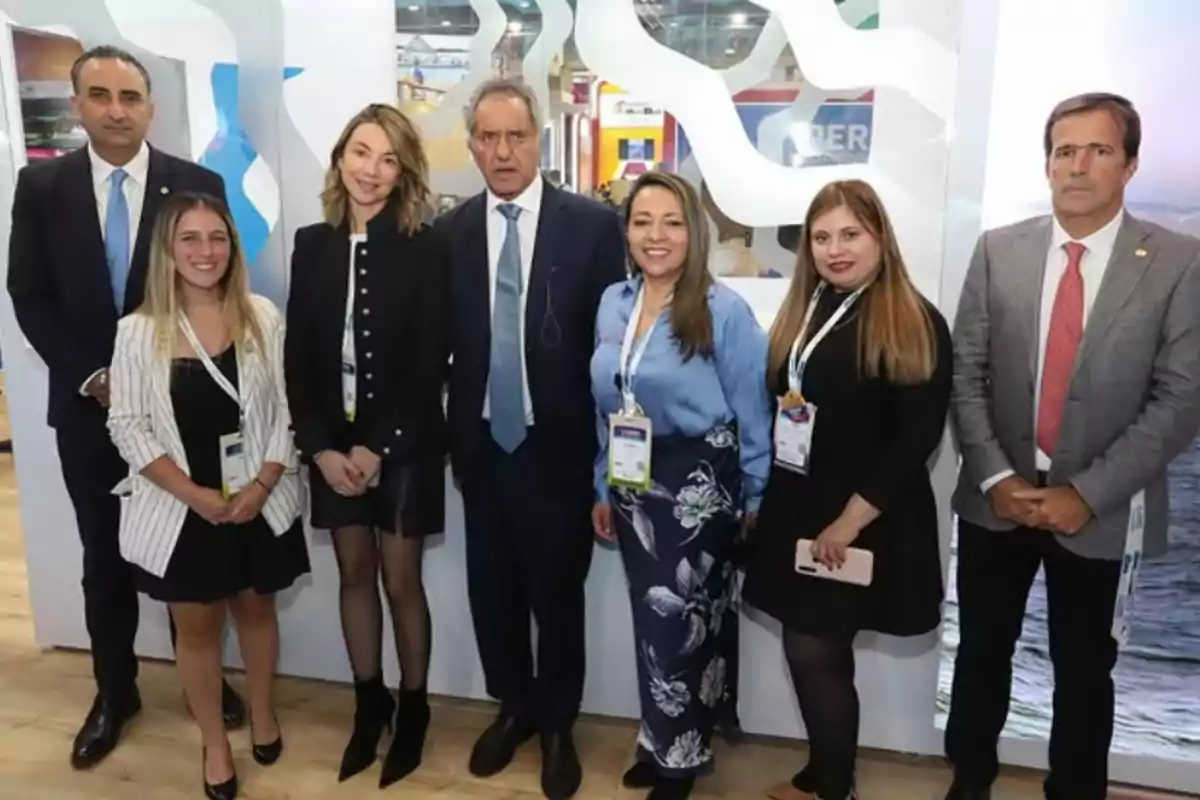 Un grupo de personas posando juntas en un evento formal, algunas llevan credenciales colgadas al cuello y están de pie frente a un fondo decorativo.