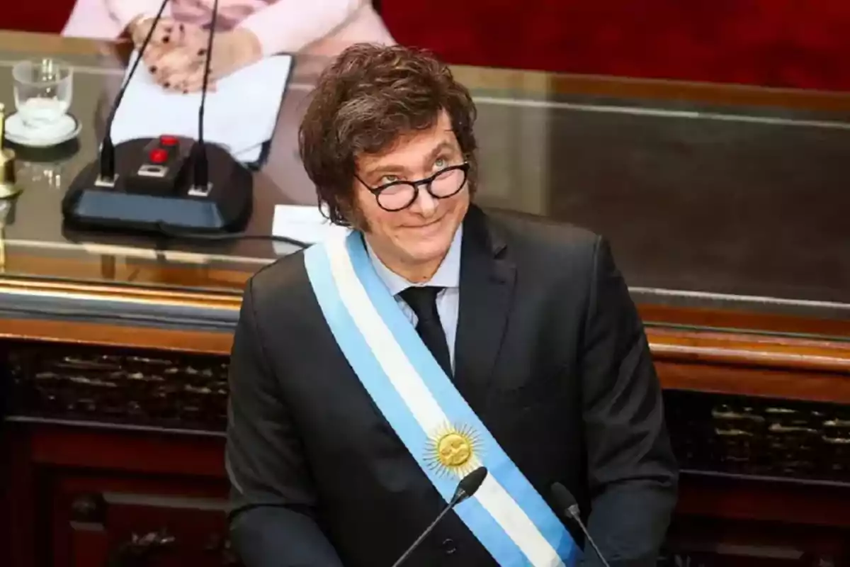 Un hombre con gafas y una banda presidencial en un entorno formal.