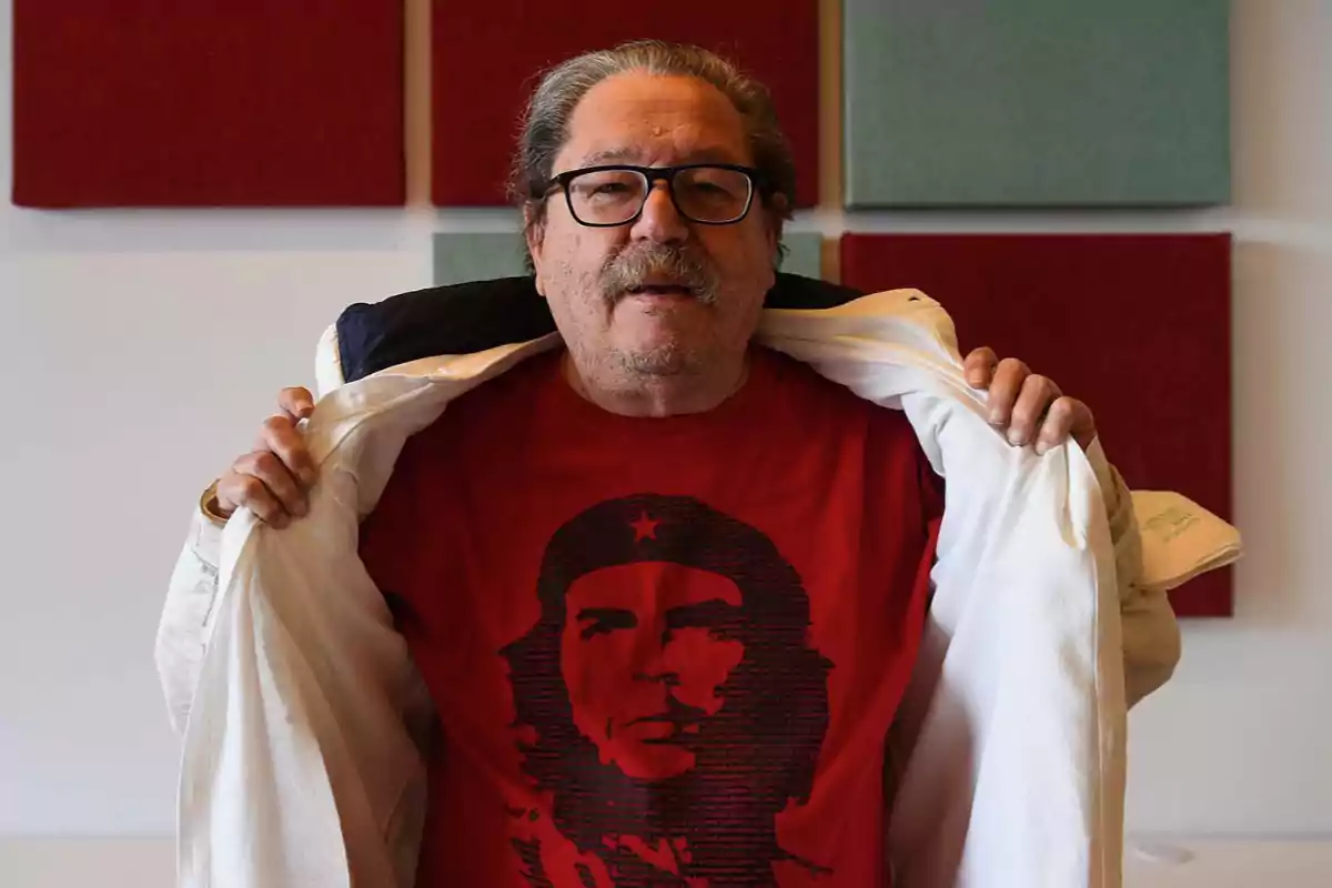 A man with glasses and a mustache displays a red T-jersey with the image of Che Guevara while holding open a white jacket.