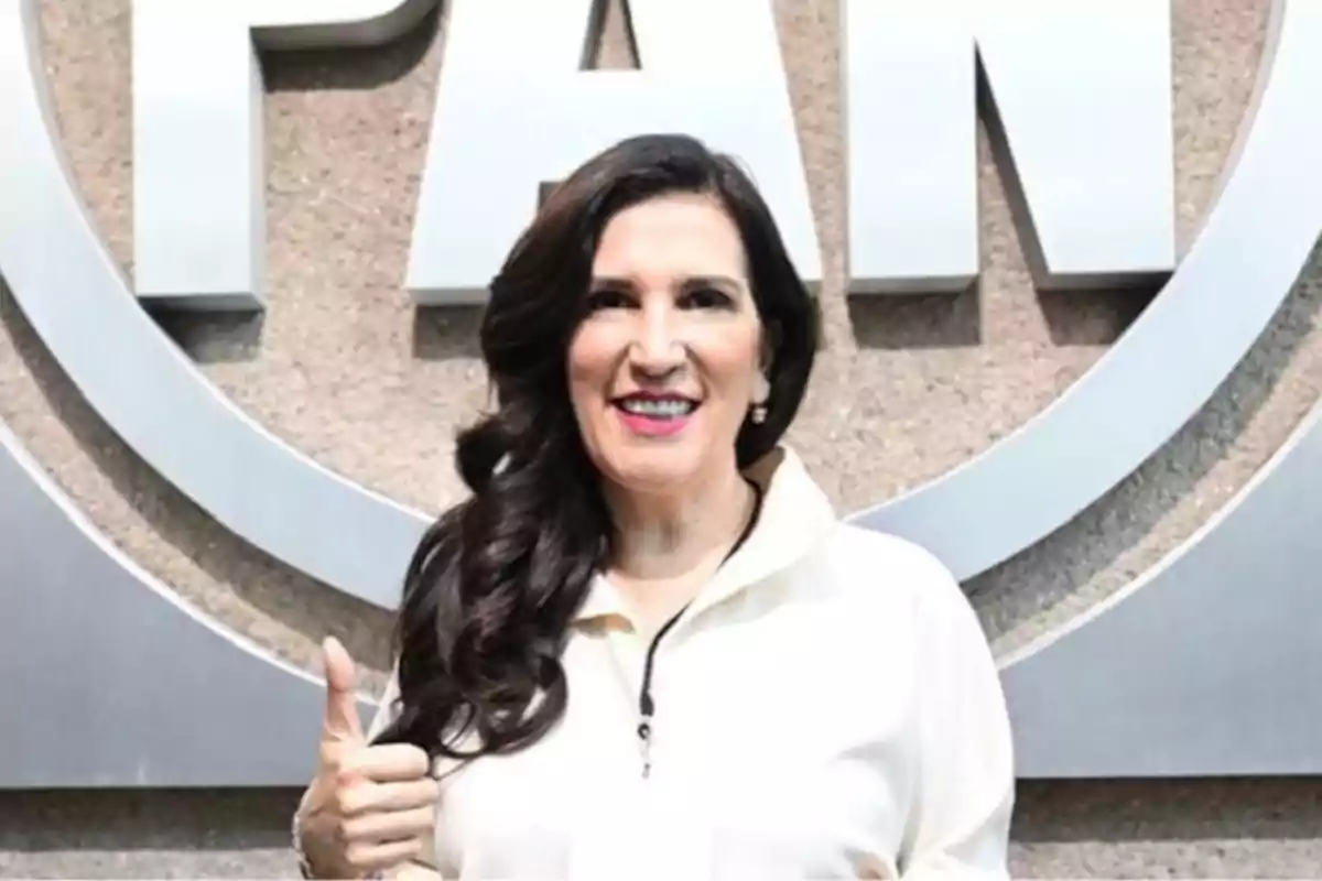 Mujer sonriendo con el pulgar hacia arriba frente a un logotipo en la pared.