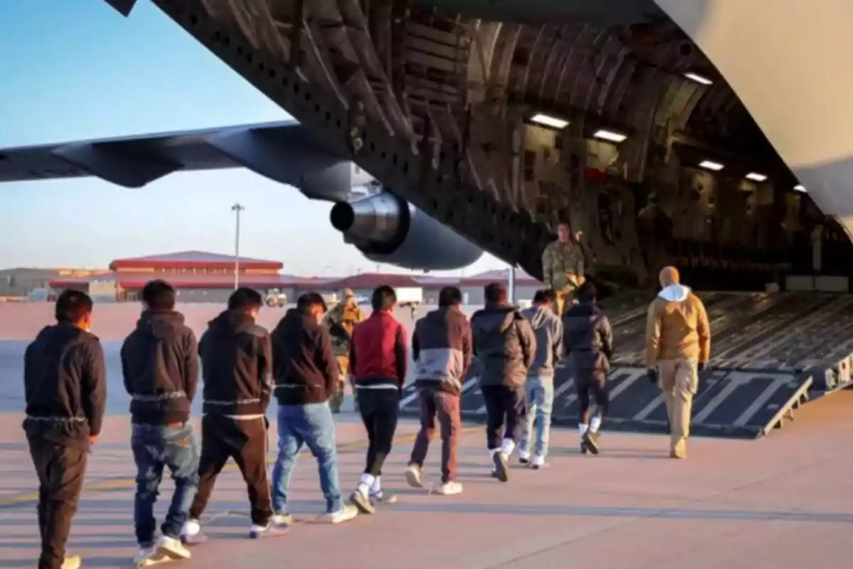 Un grupo de personas sube a un avión militar de carga en una pista de aterrizaje.