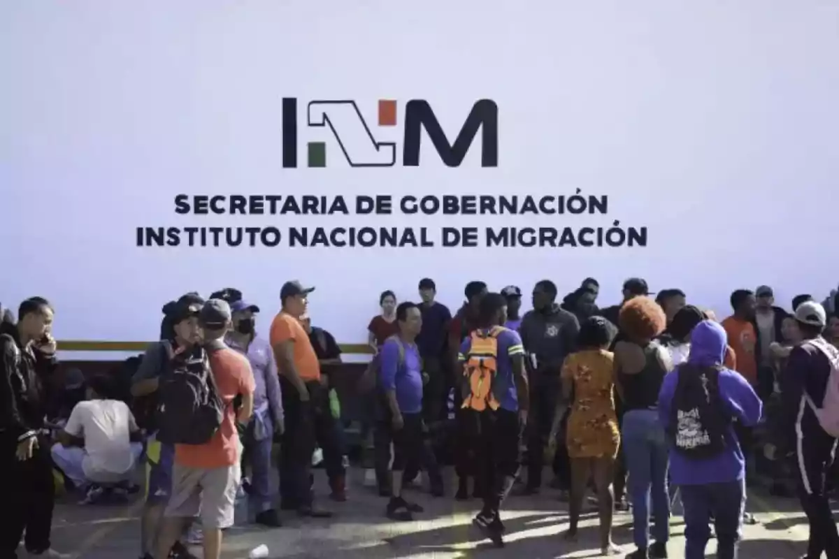 Un grupo de personas se encuentra frente a un cartel del Instituto Nacional de Migración de México.