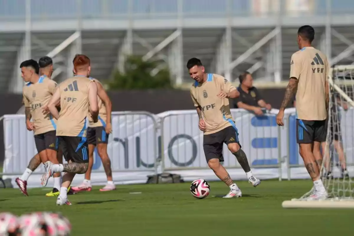 Jugadores de fútbol entrenando en un campo de césped con camisetas beige y pantalones cortos oscuros.