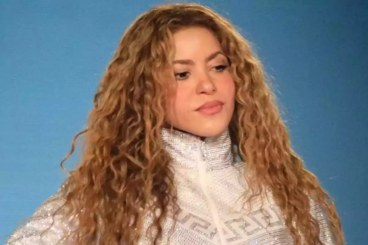 Shakira vistiendo una chaqueta brillante, sobre un fondo azul.